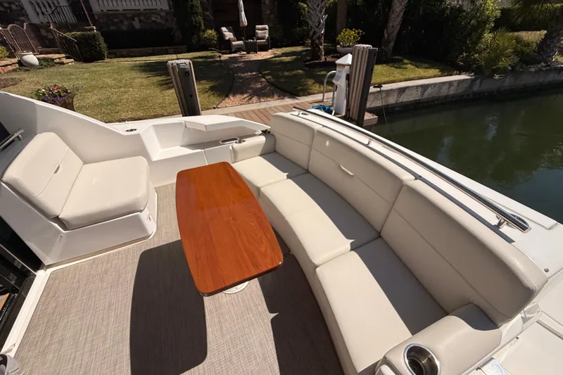 Slide: The Image of 2020 Tiara Yachts C44 Coupe cockpit with seating and wooden table, docked by a serene waterfront. - 54