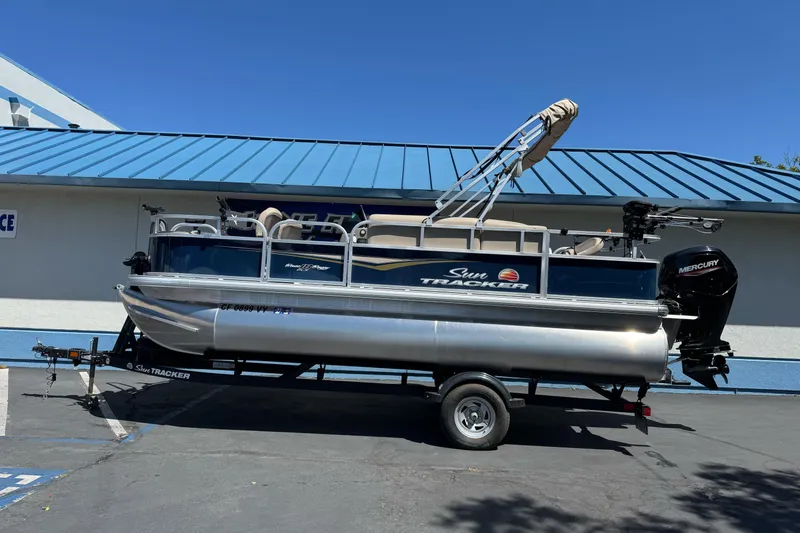 The Image of 2025 Sun Tracker Bass Buggy 18 DLX pontoon boat on trailer, parked outdoors. - 1