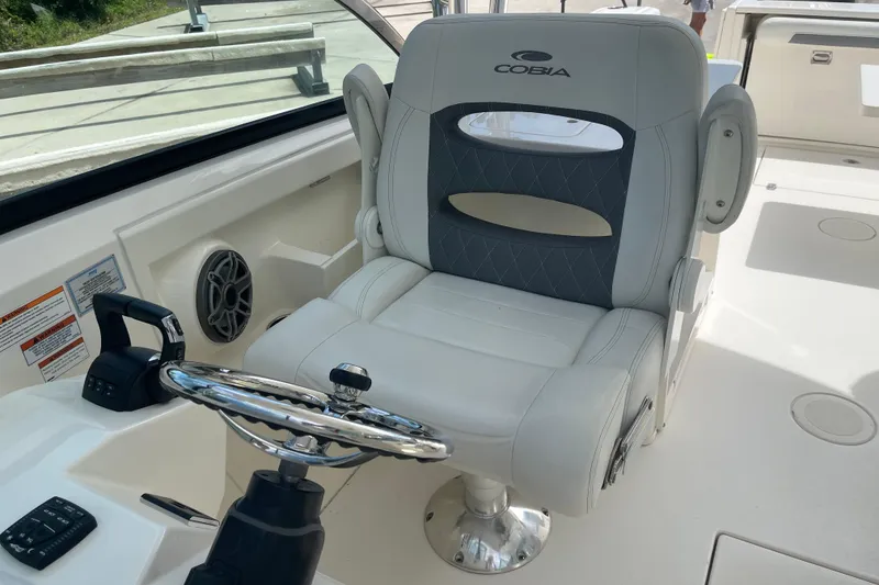 Slide: The Image of Captain's chair in 2023 Cobia 280 Dual Console boat cockpit, featuring steering wheel and controls. - 11
