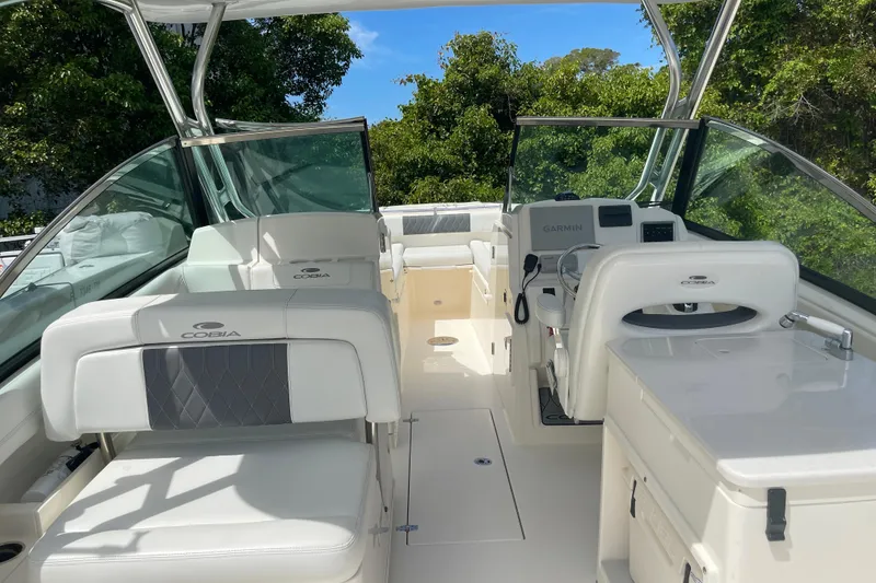 Slide: The Image of 2023 Cobia 280 Dual Console boat interior with seating and helm, surrounded by lush greenery. - 12