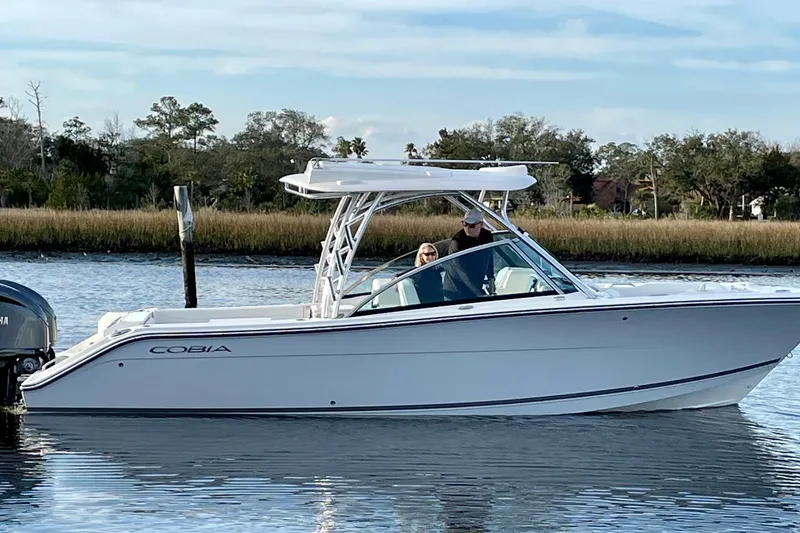 Slide: The Image of 2023 Cobia 280 Dual Console boat cruising on a calm river with scenic background. - 4