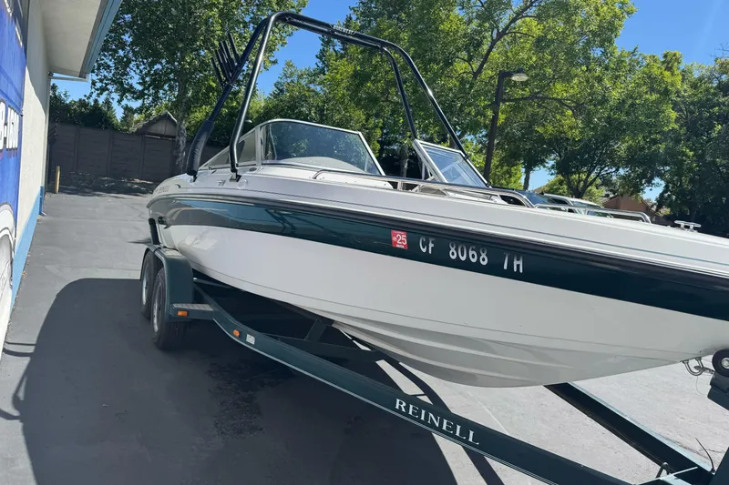 Slide: The Image of 2001 Reinell 203 boat on trailer, parked outdoors, surrounded by trees and a building. - 5