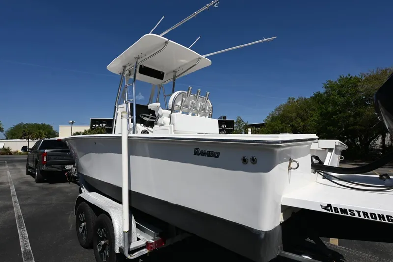 Slide: The Image of White 2017 Rambo 27 boat on trailer in parking lot under clear blue sky. - 17