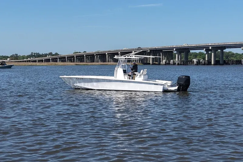 Slide: The Image of A 2017 Rambo 27 boat on calm water near a bridge under a clear blue sky. - 2