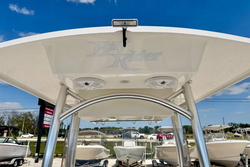 Slide: The Image of 2026 Bay Rider 219 Bay boat with T-top and speakers, under clear blue sky. - 45