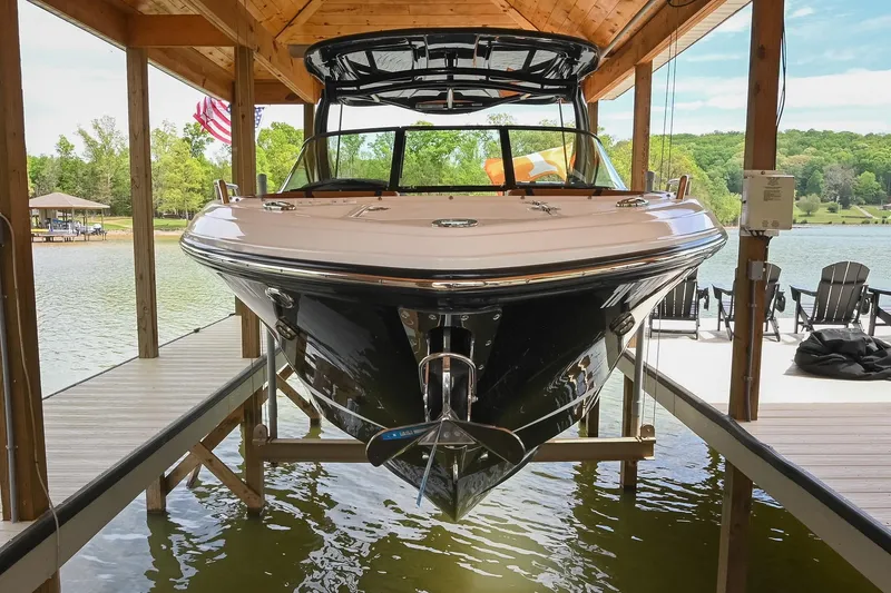 Slide: The Image of 2022 Chaparral 307 SSX boat docked under a wooden canopy on a serene lake. - 2