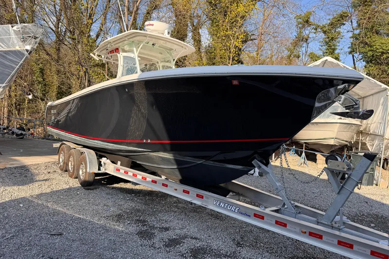 Slide: The Image of 2015 Sailfish 320 CC boat on trailer, parked outdoors with trees in background. - 2