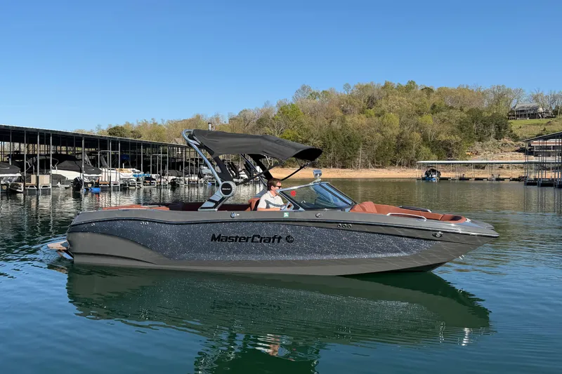 The Image of 2021 MasterCraft X24 boat on a calm lake with docks and trees in the background. - 0