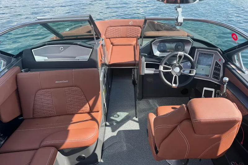 Slide: The Image of 2021 MasterCraft X24 boat interior with brown leather seats and modern dashboard on water. - 10