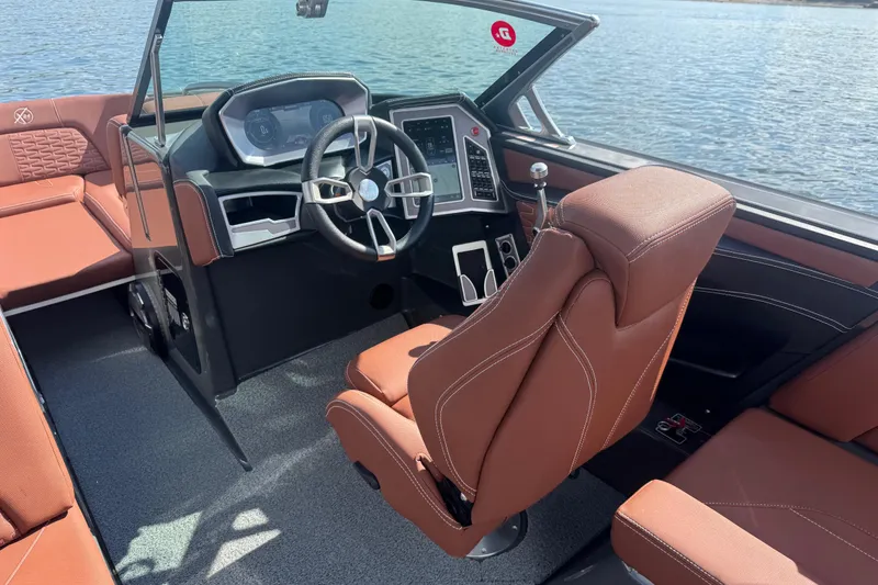 Slide: The Image of 2021 MasterCraft X24 boat interior with brown seating and modern dashboard on water. - 11