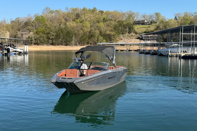 Slide: The Image of 2021 MasterCraft X24 boat cruising on a serene lake near docks and wooded shoreline. - 4