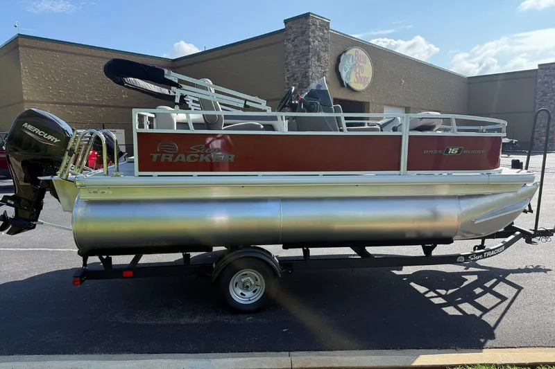 The Image of 2026 Sun Tracker Bass Buggy 16 XL Select pontoon boat on trailer, parked outside store. - 0