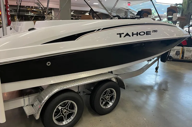Slide: The Image of 2026 Tahoe 2150 boat on trailer in showroom, sleek black and white design. - 3