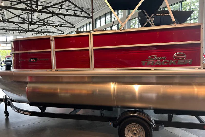 Slide: The Image of 2026 Sun Tracker Party Barge 16 DLX pontoon boat in showroom, featuring red exterior and trailer. - 1