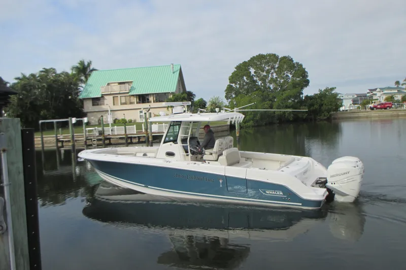 Slide: The Image of 2018 Boston Whaler 330 Outrage boat cruising on calm water near a waterfront home. - 2