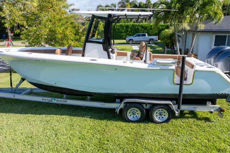 Slide: The Image of 2021 Sea Hunt Gamefish 27 boat on trailer, parked on grass, surrounded by trees. - 63