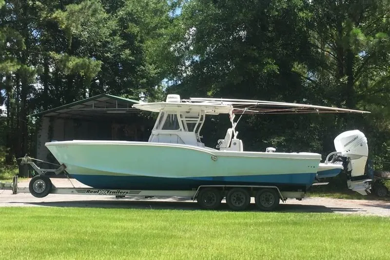 Slide: The Image of 1999 Ocean Master 31 boat on trailer, parked outdoors with trees in background. - 15