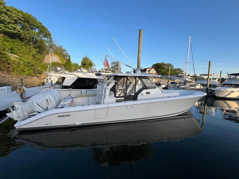 Slide: The Image of 2019 Pursuit S 408 Sport boat docked in a marina, reflecting on calm water. - 14