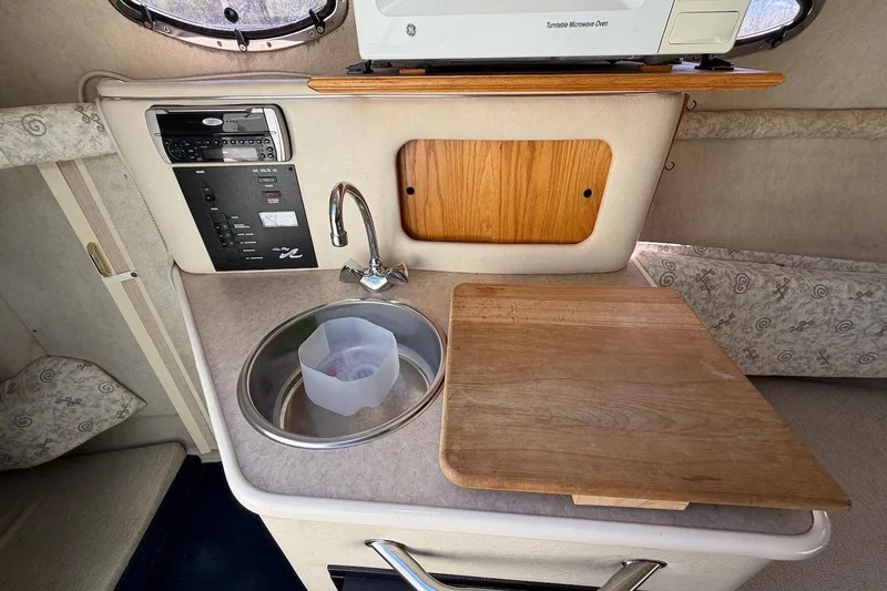 Slide: The Image of 2002 Sea Ray 240 Sundancer cabin kitchenette with sink, cutting board, and microwave. - 26