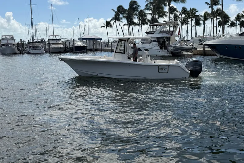 Slide: The Image of 2022 Sea Hunt Ultra 275 SE boat cruising in a marina with palm trees and yachts. - 2