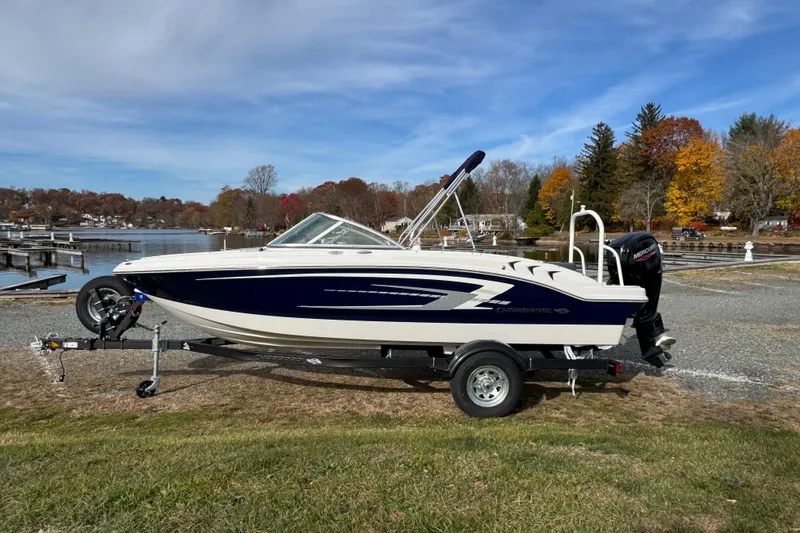 Slide: The Image of 2026 Chaparral 19 SSi OB boat on trailer by lakeside, autumn trees in background. - 2