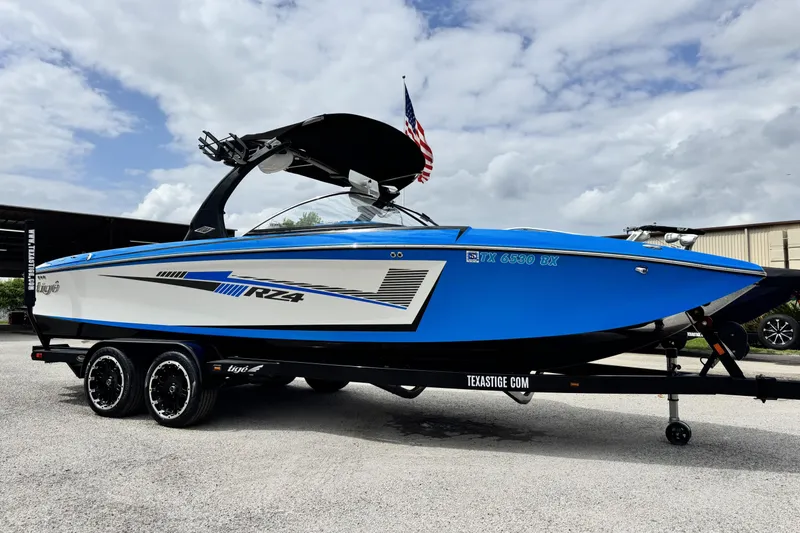The Image of 2013 Tigé RZ4 boat in blue and white on a trailer, under a cloudy sky. - 1