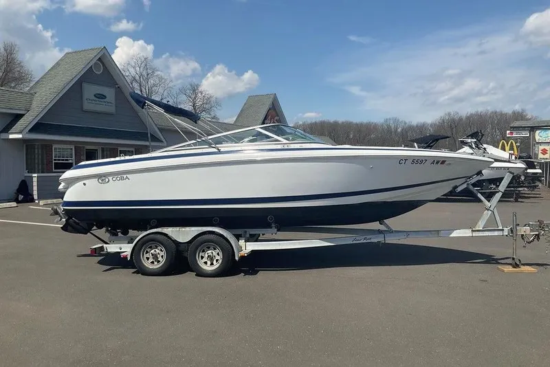 The Image of 2000 Cobalt 226 boat on trailer, parked outside a building under a partly cloudy sky. - 0