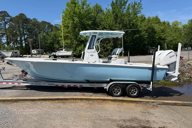 Slide: The Image of 2024 Tidewater 2700 Carolina Bay boat on trailer, parked near lush greenery. - 19