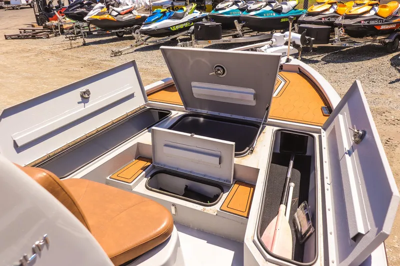 Slide: The Image of 2024 Avid 21 FSX boat interior with open storage compartments and nearby jet skis. - 13