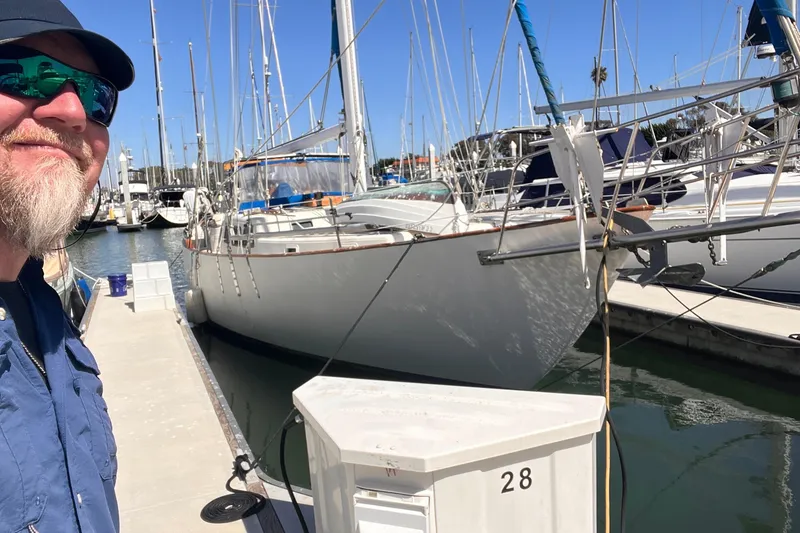 Slide: The Image of Man smiling beside 1983 Westsail 42 Center Cockpit sailboat docked at marina. - 2