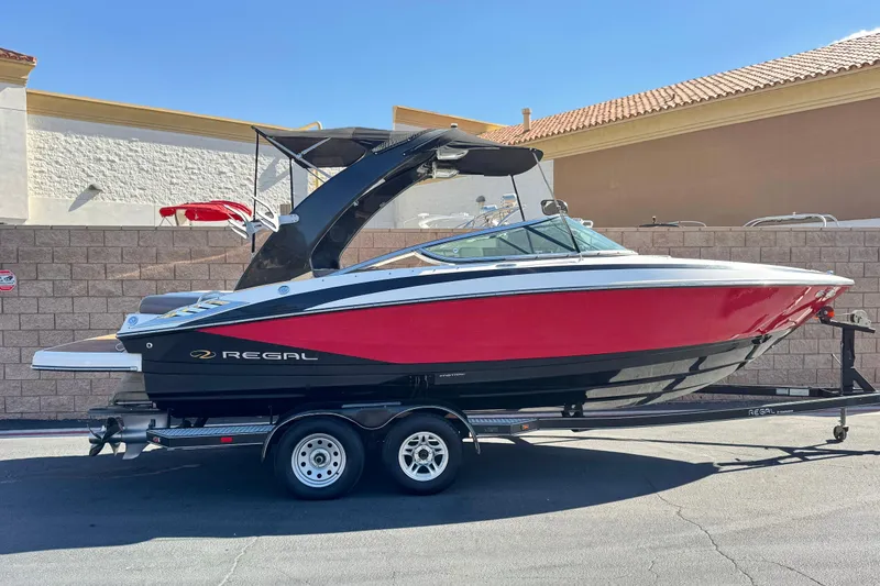 The Image of 2010 Regal 2300 RX Bowrider boat on trailer, red and black design, parked outdoors. - 0