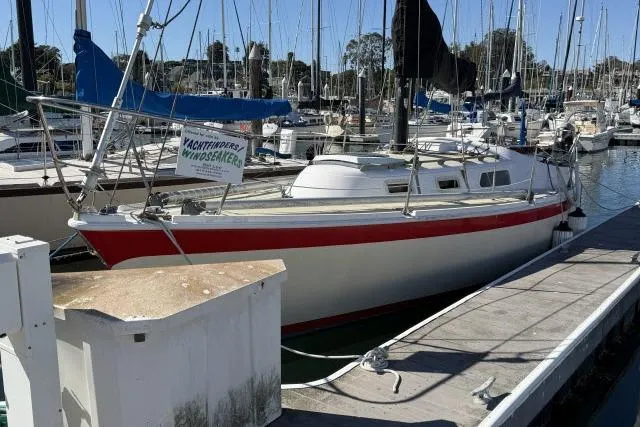 Slide: The Image of 1976 CAL 3-30 sailboat docked in marina, featuring red stripe and white hull. - 17