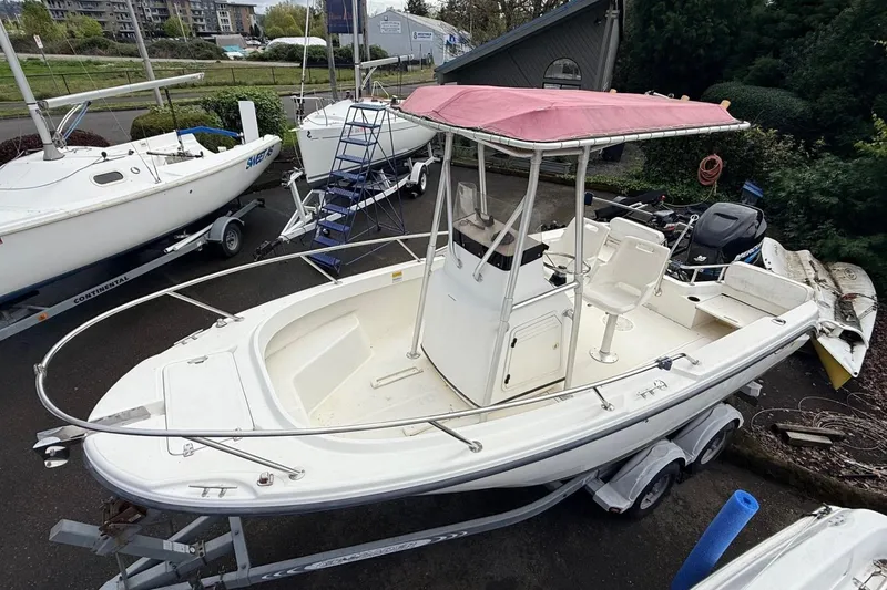 The Image of 1999 Boston Whaler Outrage 18 boat with red canopy on trailer, parked near other boats. - 1