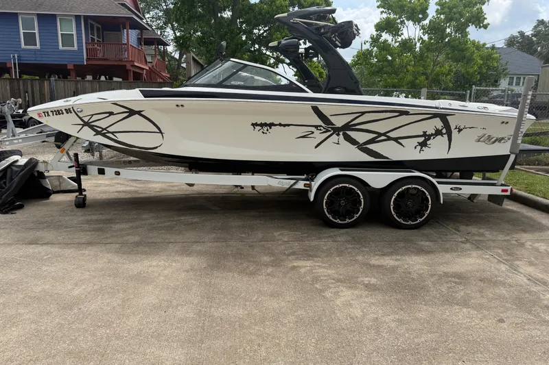 The Image of 2010 Tigé RZ2 boat on trailer, white with black graphics, parked in residential driveway. - 0