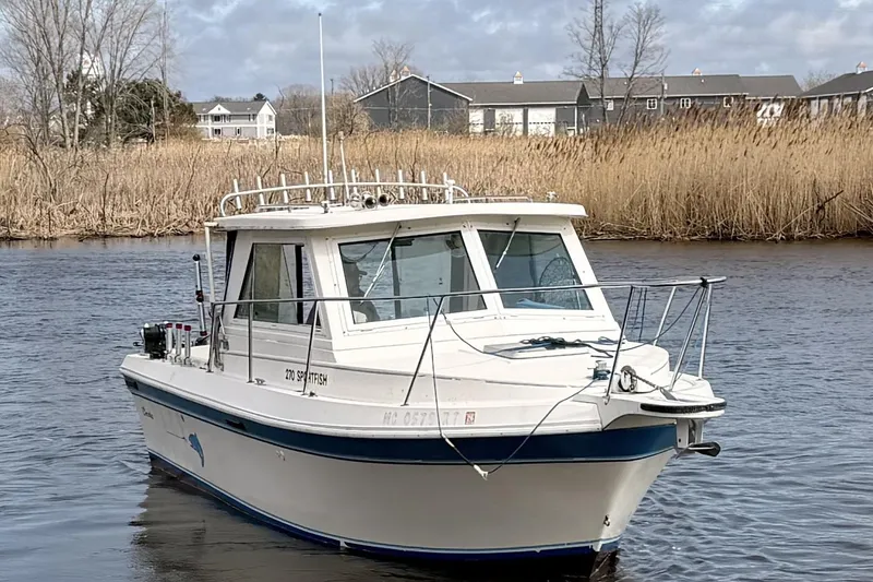 Slide: The Image of 1998 Cherokee 270 Sportsman boat on a calm river with reeds and houses in the background. - 2