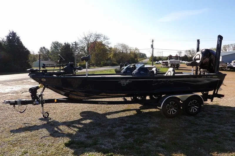 Slide: The Image of 2026 Lund 2075 Pro-V Bass XS boat on trailer, parked outdoors in a sunny setting. - 12