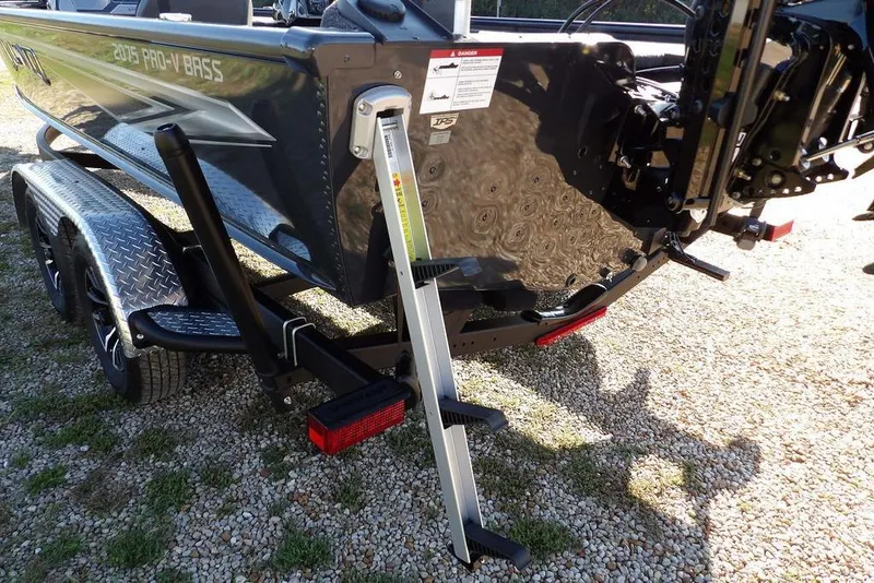 Slide: The Image of 2026 Lund 2075 Pro-V Bass XS boat on trailer with ladder, parked on gravel. - 34