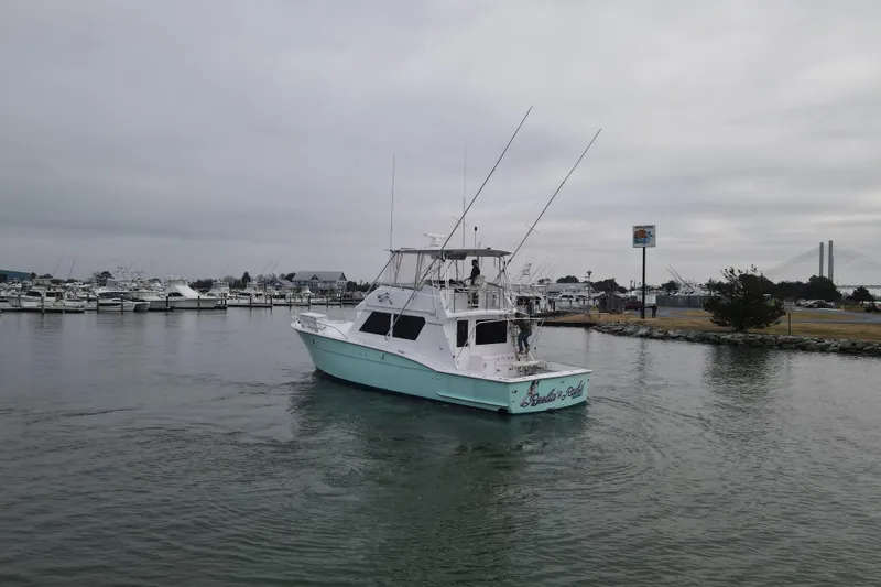 Slide: The Image of 1989 Hatteras 52 Convertible yacht cruising near marina under cloudy skies. - 5