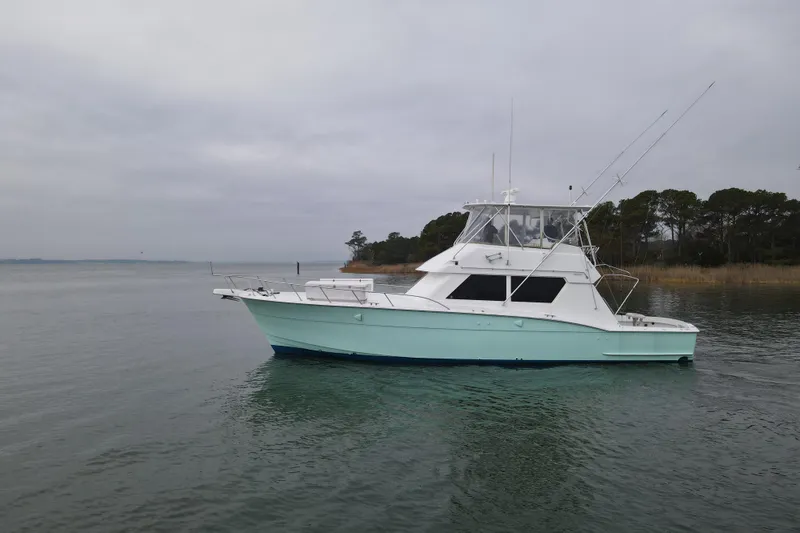 Slide: The Image of 1989 Hatteras 52 Convertible yacht on calm waters near a wooded shoreline. - 4