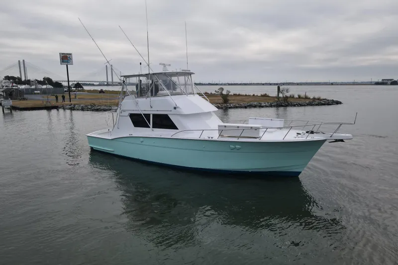 Slide: The Image of 1989 Hatteras 52 Convertible yacht on calm water near a bridge and shoreline. - 1
