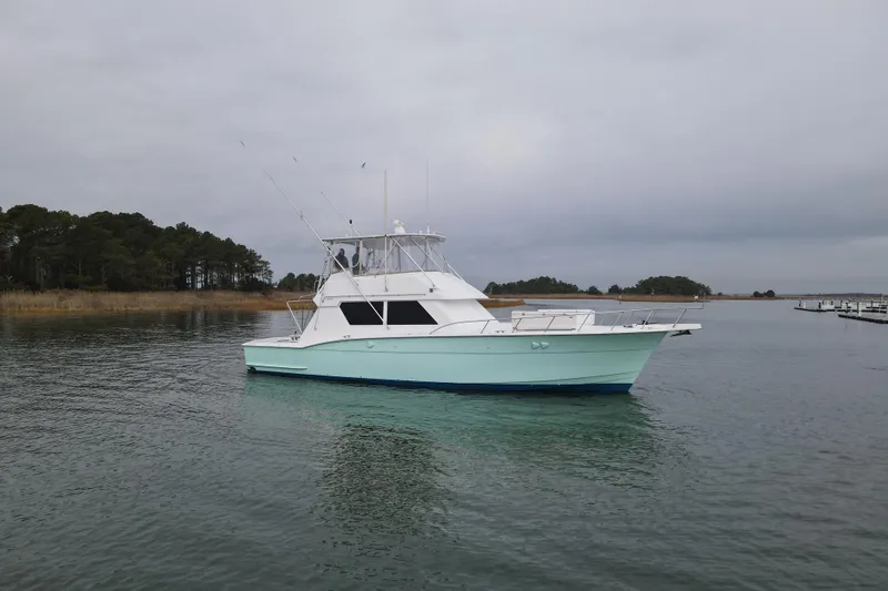Slide: The Image of 1989 Hatteras 52 Convertible yacht on calm water, overcast sky, near shoreline. - 2