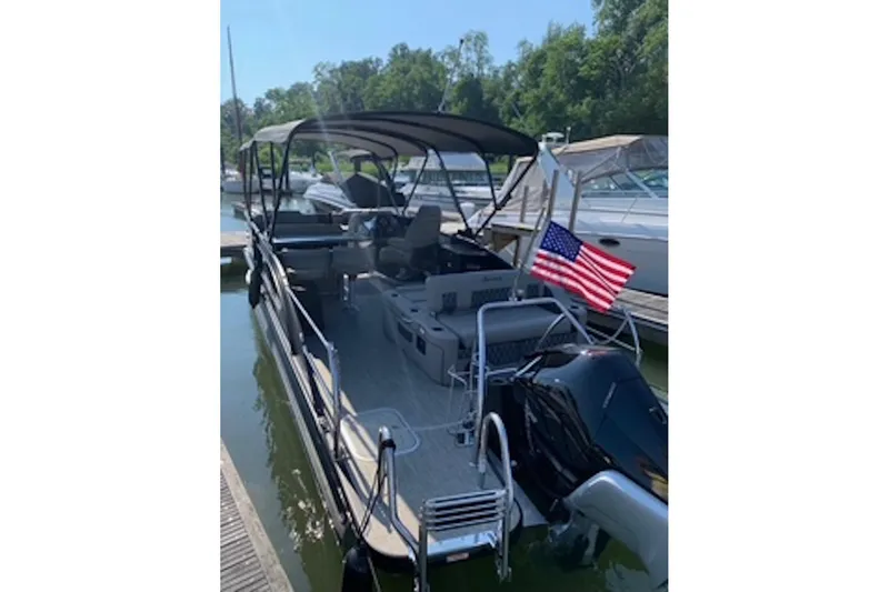 Slide: The Image of 2021 Barletta L25UE pontoon boat docked with American flag, surrounded by trees. - 4