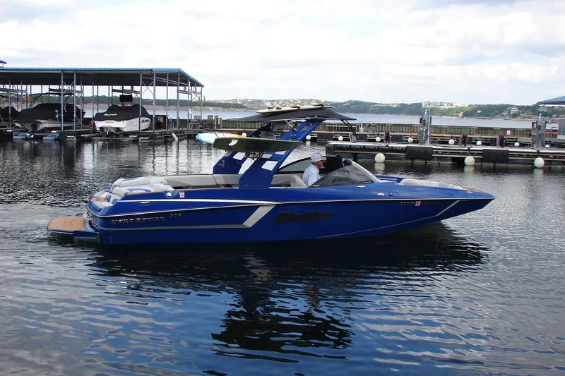 Slide: The Image of 2017 Malibu Wakesetter 24 MXZ boat docked on calm water, blue exterior. - 12