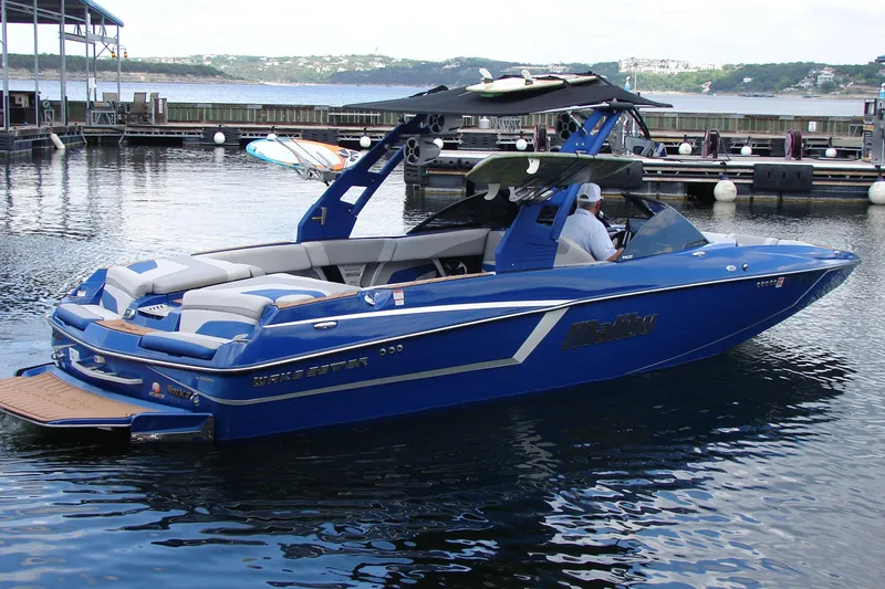 Slide: The Image of 2017 Malibu Wakesetter 24 MXZ boat docked on calm water, featuring sleek blue design. - 13