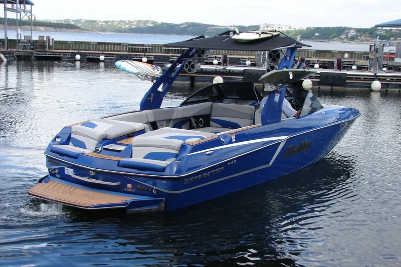Slide: The Image of 2017 Malibu Wakesetter 24 MXZ boat in blue, docked on a calm lake. - 14