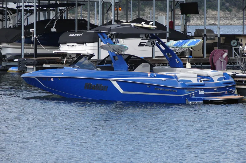 Slide: The Image of 2017 Malibu Wakesetter 24 MXZ boat docked in marina, vibrant blue color. - 2
