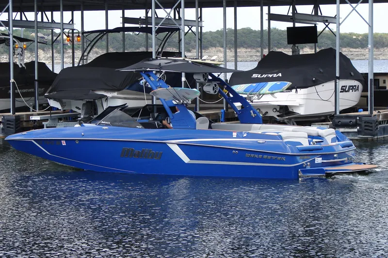 Slide: The Image of 2017 Malibu Wakesetter 24 MXZ boat docked in marina, vibrant blue color. - 6