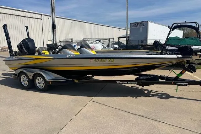 Slide: The Image of 2008 Triton 21X2 DC boat on trailer, parked outdoors near industrial building. - 12