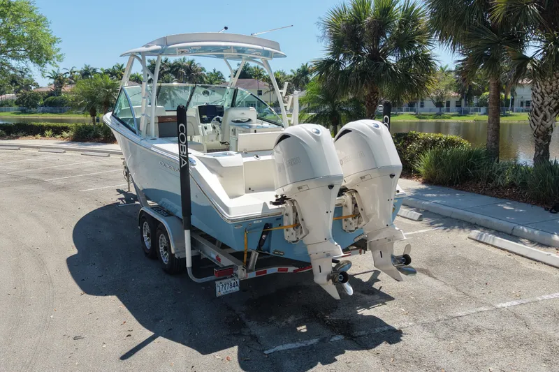 Slide: The Image of 2021 Cobia 280 Dual Console boat on trailer, parked near palm trees. - 2