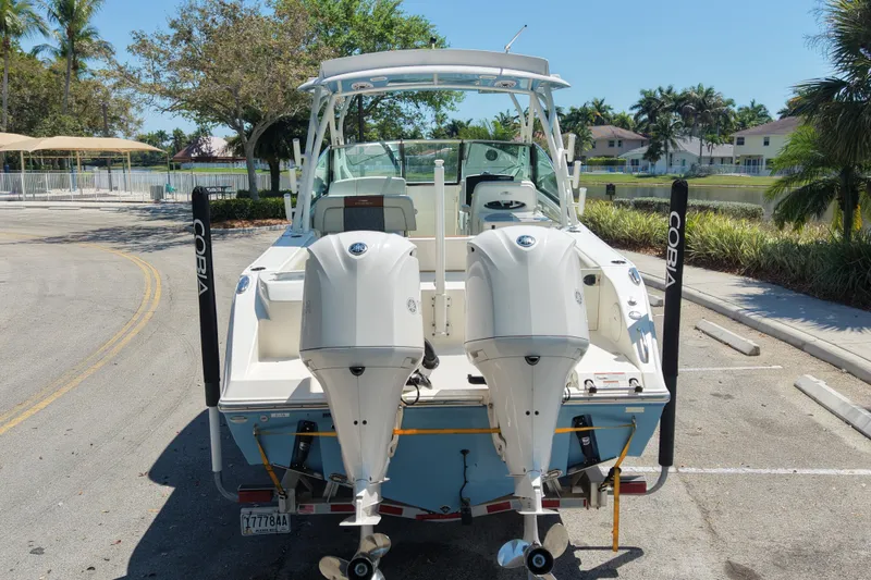 Slide: The Image of 2021 Cobia 280 Dual Console boat with twin outboard engines in a sunny parking area. - 5